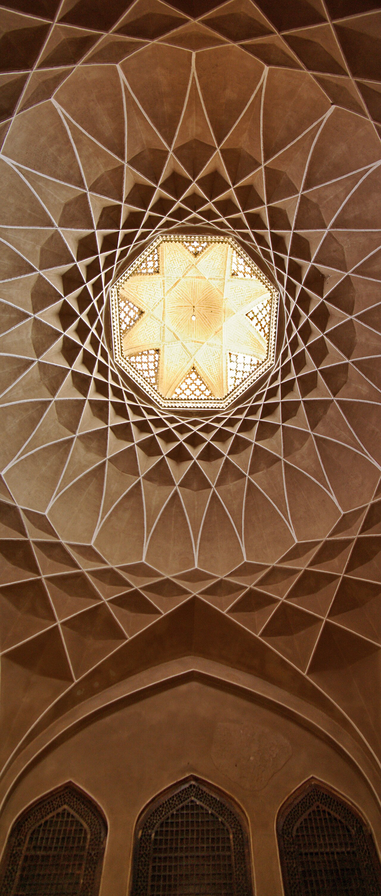 A 33-metre badgir (wind-catcher) of Yazd — the tallest passive cooling tower in the world, drawing dry air down across a basement qanat pool to chill the rooms below.