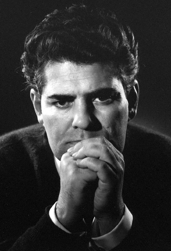 A black and white photograph of an elderly Ahmad Shamlou, looking thoughtfully towards the viewer, his face lined with age and a cigarette held between his fingers.