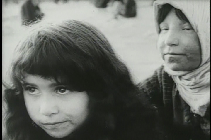 A stark black and white film still from 'The House is Black' showing residents of the leper colony, their faces marked by the disease, looking directly at the camera with dignity.